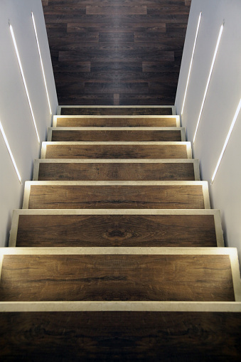 Symmetric wooden staircase downwards, illuminated with led stripes on the wall