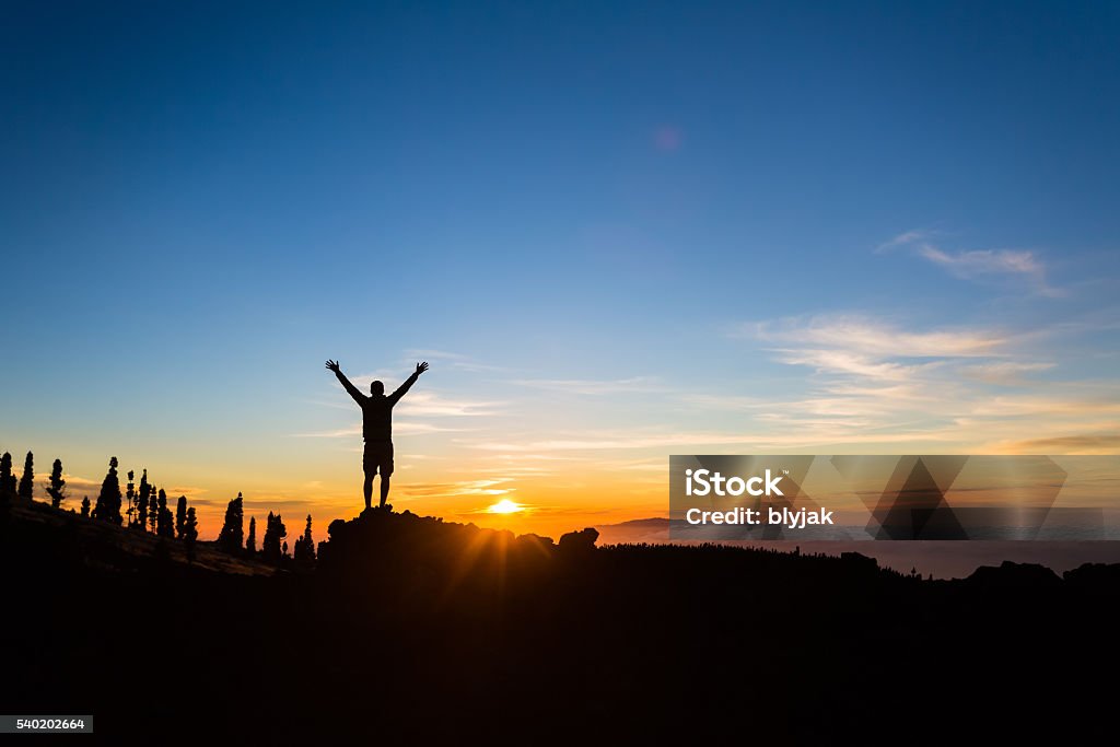 Man hiker silhouette with arms outstretched enjoy mountains Man hiker silhouette with arms outstretched in mountains. Male runner or climber looking at sunset view. Business concept and hands up and enjoy inspirational landscape, rocky trail footpath on Tenerife, Canary Islands Mountain Stock Photo