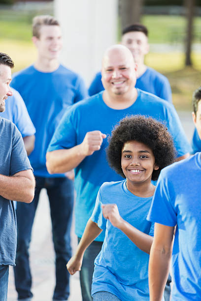 Mixed race boy running with a team of men A mixed race African American and Pacific Islander 12 year old boy running with a group of men. They are part of a team, wearing blue shirts and jeans. They are supporting a cause. walking for a cause stock pictures, royalty-free photos & images