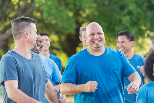 A multi-ethnic group of men in the park wearing blue t-shirts. They are a team of volunteers standing together.  The focus is on an Hispanic bald man in his 40s.