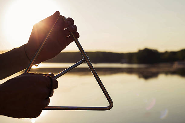 Playing a musical instrument triangle on background sky at sunset Minsk, Belarus - June, 2016: Playing a musical instrument triangle on background sky at sunset castanets stock pictures, royalty-free photos & images