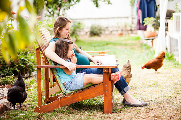 Pregnant Woman Reading to Daugther in Backyard Attractive young pregnant woman reads to her daughter in the back yard, while chickens peck around and laundry hangs in the background. chickens in the poultry yard eating stock pictures, royalty-free photos & images
