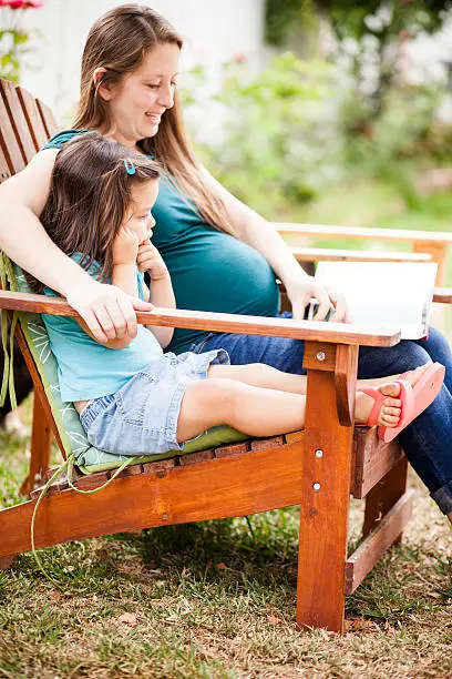 Photo of Pregnant Woman Reading to Daugther in Backyard