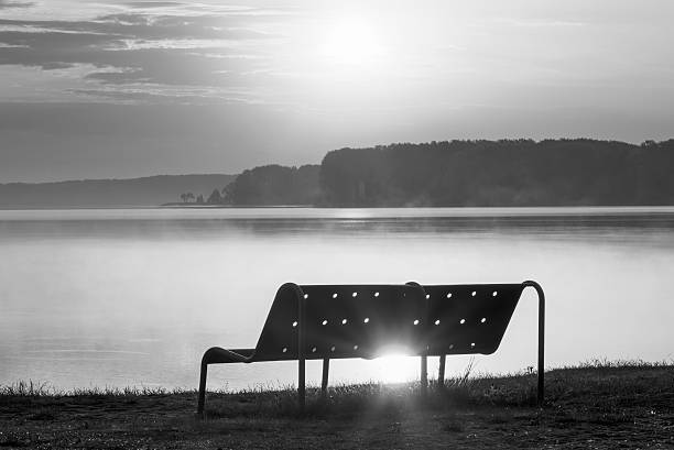 пустые скамейке на озеро пляж на рассвете, черно-белый - sea black and white horizontal horizon over water стоковые фото и изображения