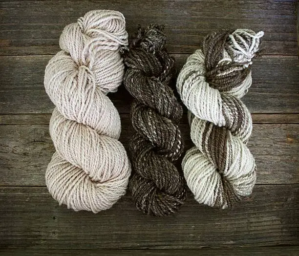 Three skeins of brown and beige handspun yarn on a wood surface.