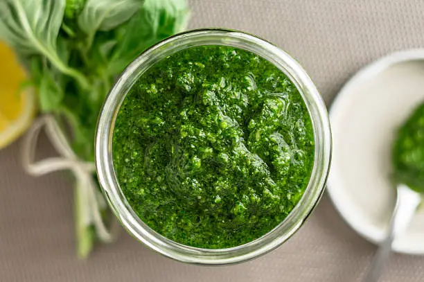 Fresh homemade basil pesto sauce in a glass jar viewed from above. Originally from italy, pesto is commonly made with basil and used as a sauce for pasta.