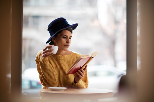 Serious young woman drinking coffee and reading a book in a cafe.