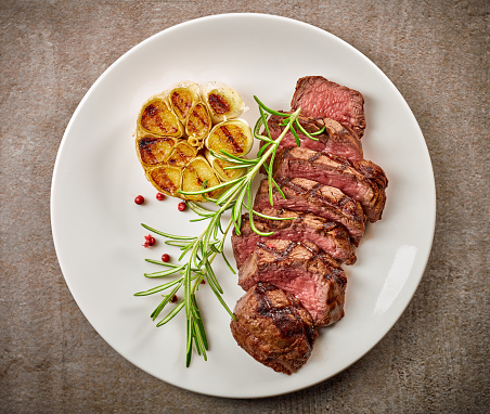 grilled sliced steak and rosemary on white plate, top view