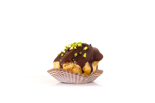 Petit four: a mini chocolate cream puff/eclair with pistachio sprinkles on a white background. Copy space available.