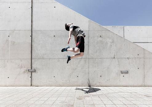 Young man jumping in front of concrete wall