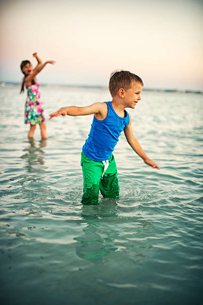 les enfants portant des vêtements jouant dans l'eau de mer - wading child beach sundress photos et images de collection