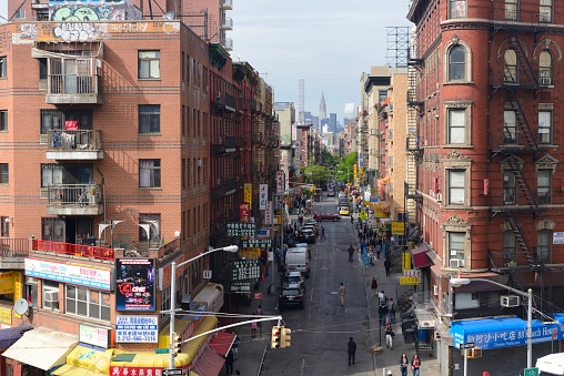 New York, USA - May 18, 2016: Division Street in Chinatown as seen from the Manhattan Bridge. Division Street is a one-way street in the Lower East Side of the New York City borough of Manhattan. It runs in a northeasterly direction with westbound traffic and passes beneath the Manhattan Bridge. It is a mostly residential street. You can see a lot of outdoor advertisements. Some people are walking on the street. On the foreground is Forsyth Street. Far away are the Chrysler building and 432 Park Avenue.