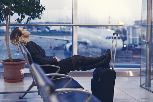 side view of young woman trying to rest inside airport lounge, lying on the chair and waiting, sleeping.