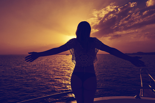 rear view of woman silhouette in the sunset holding her arms raised and feeling the great freedom feeling.