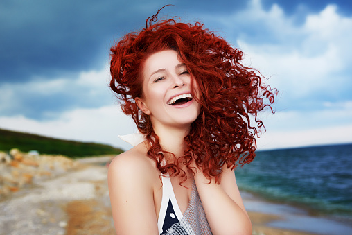 lifestyle shot of happy young curly hair woman laughing and feeling great in her vacation, looking at camera.