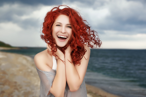 happy young woman on the beach enjoying her day and laughing, feeling amazing in her vacation,red curly hair.