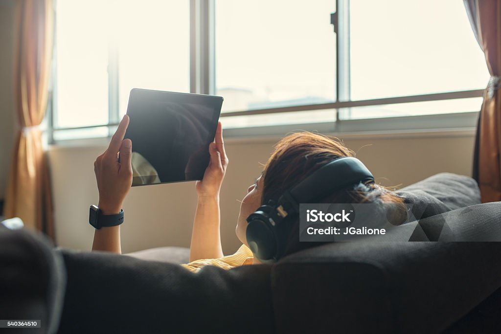 Young woman using digital tablet Young adult woman relaxing on a sofa using a digital tablet. Kyoto, Japan. May 2016 Downloading Stock Photo