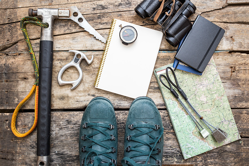 Climbing tools with boots and notebook on wooden background. Ice axe, nuts, compass, mountain boots and map lying on wood board