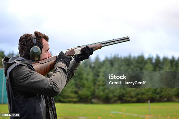 Man Shooting Shotguns At Clay Pigeon Outdoors Stock Photo - Download Image Now - Target Shooting, Shooting a Weapon, Taking a Shot - Sport