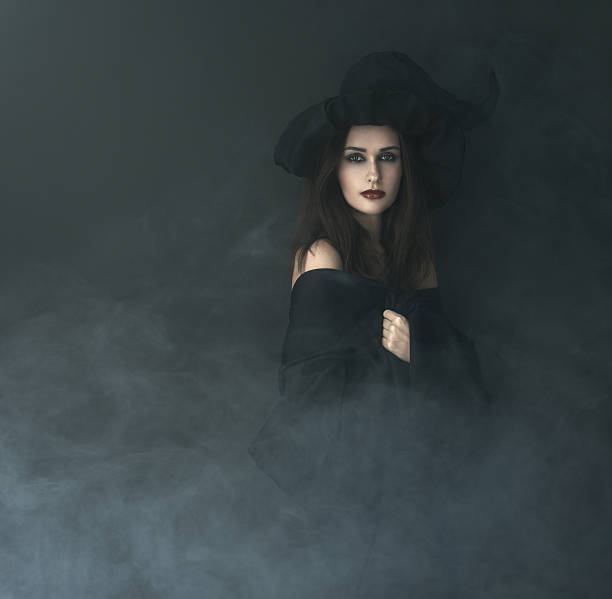 slender witch in a smoke on  black background stock photo