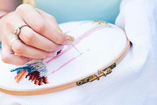 Female hand embroiders angels in the hoop, Young girl embroiders a pattern on the white material, sweetie brunette engaged in needlework