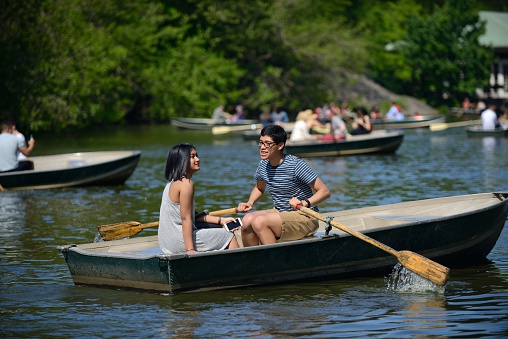 New York, USA - May 20, 2016: Couple enjoying themselves in a rowboat on the Central Park lake. On the background you can see more people rowing boats.