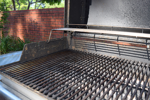 This is a dirty metal grate of an outdoor barbecue grill with bits of food stuck on it.