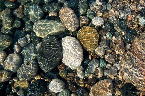 Ripples on the water surface in shallow water with colourful stones.