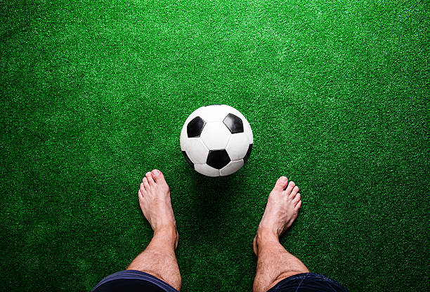 Legs of unrecognizable barefoot football player against artificial grass. Studio shot on green grass.