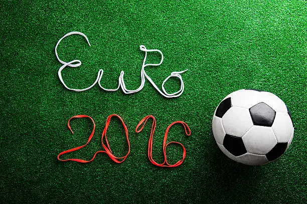 Soccer ball and Euro 2016 sign made of shoelaces against artificial turf, studio shot on green background. Flat lay.