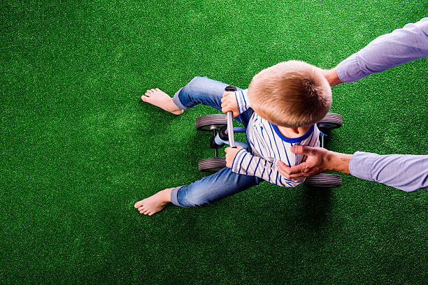 irreconocible padre sostiene un su hijo montar una bicicleta - child human foot barefoot jeans fotografías e imágenes de stock