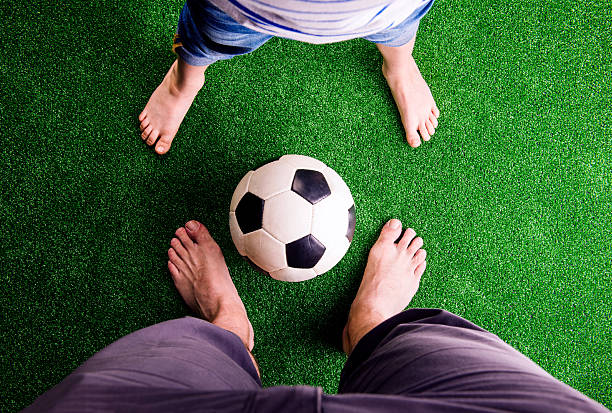 padre e hijo con balón de fútbol con césped verde - child human foot barefoot jeans fotografías e imágenes de stock