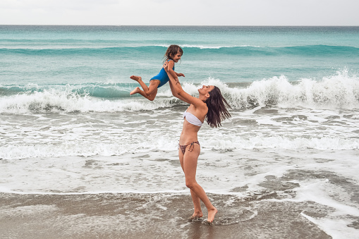 Woman raises young child up above her head beachside