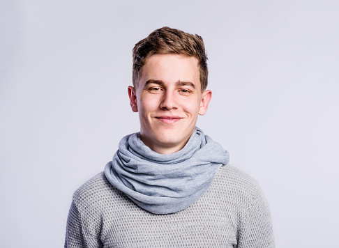 Teenage boy in gray sweater and scarf, young man, studio shot on gray background