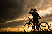 Silhouette of cyclist drinking water on the top of mountain