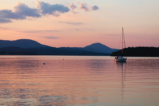 Pink light sunset on vermont lake with sailboat