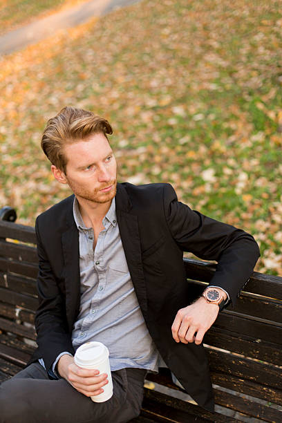 istock Young man on bench drinking coffee at autumn park 540499666