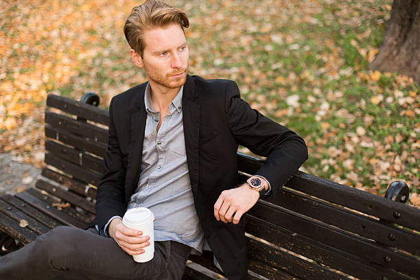 istock Young man on bench drinking coffee at autumn park 540499686