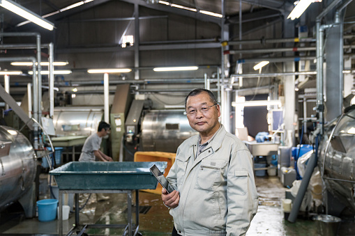 Confident senior textile industry manager holding a digital tablet in a garment factory