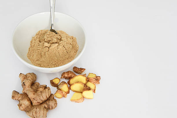 Ginger powder in bowl with metal spoon, ginger root, isolated stock photo