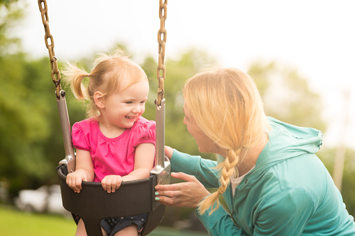 Pretty toddler girl on swing smiling at her mother.