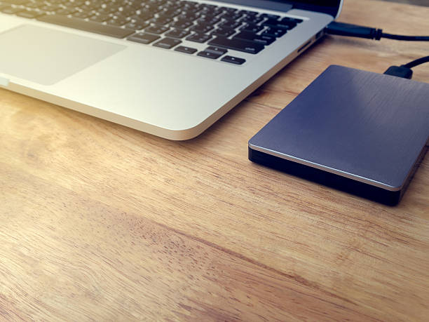 External hard drive connected to laptop computer External or portable hard drive (HDD) connected to laptop computer for transfer or backup data on wooden texture office desktop with copy space solid state disk photos stock pictures, royalty-free photos & images