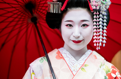 Portrait of a beautiful Maiko girl outdoors holding an umbrella and smiling