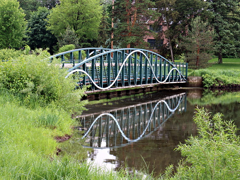 Blue footbridge made of iron and wood reflecting in still waters of a pond at Lake Calhoun nature area.  Photo shot in Minneapolis, Minnesota on a cloudy, rainy day.