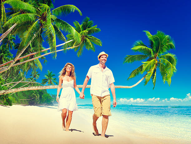 Beautiful couple in white summer clothes walks along a tropical beach and enjoys the together time