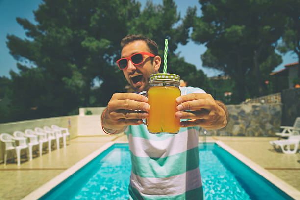 Young man on the swimming pool holding jar with orange juice.