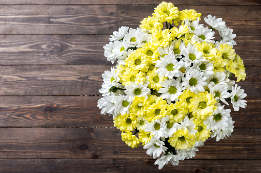 Flower bunch from small yellow and white chrysanthemums. Top view. Studio shooting on a dark-brown background of wooden floor