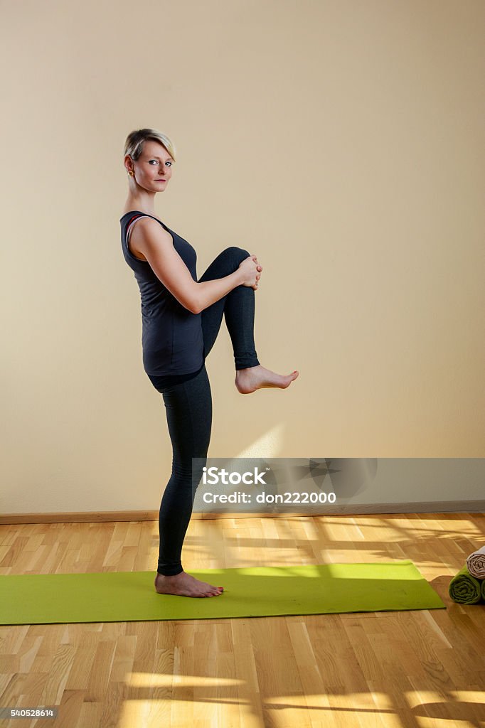 Woman doing yoga while standing on yoga mat Woman who does yoga while standing on yoga mat Active Lifestyle Stock Photo