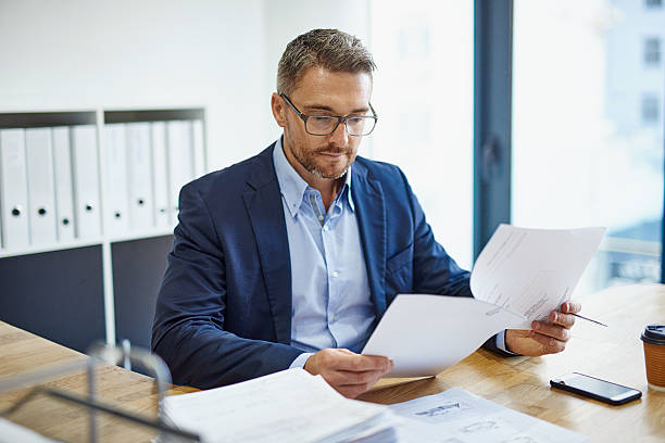 Blazing through his paperwork Shot of a mature businessman reading a document at his desk in an office report document stock pictures, royalty-free photos & images
