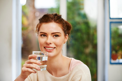 Shot of a young woman drinking a glass of water at home